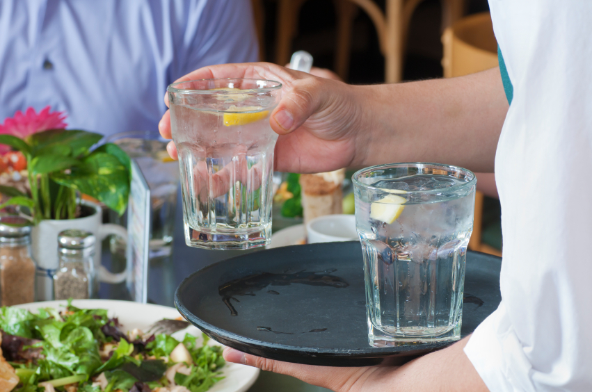 Waiter holding tray with tap water handing to customer