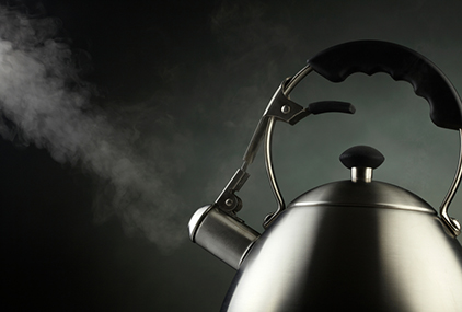 Tea kettle with boiling water over dark background
