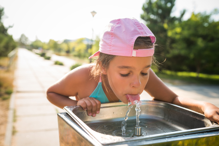 Toddler drinking from the water fountain in the summertime