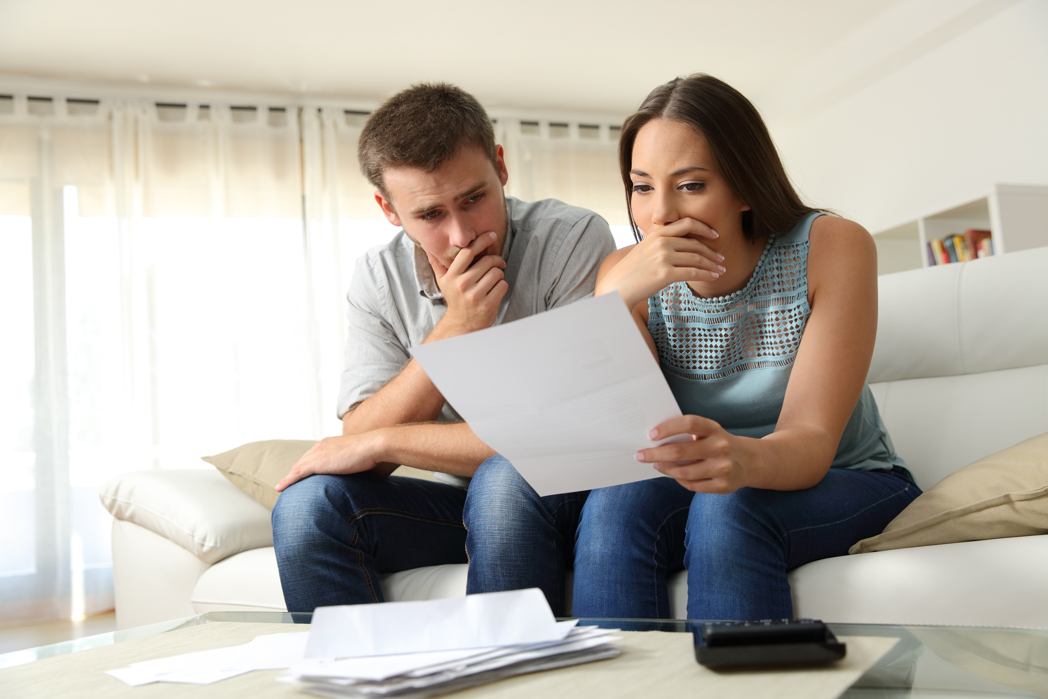 Worried couple reading a letter sitting on a couch in the living room at home