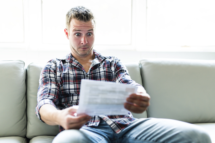 Shocked man holding a bill statement on sofa livingroom