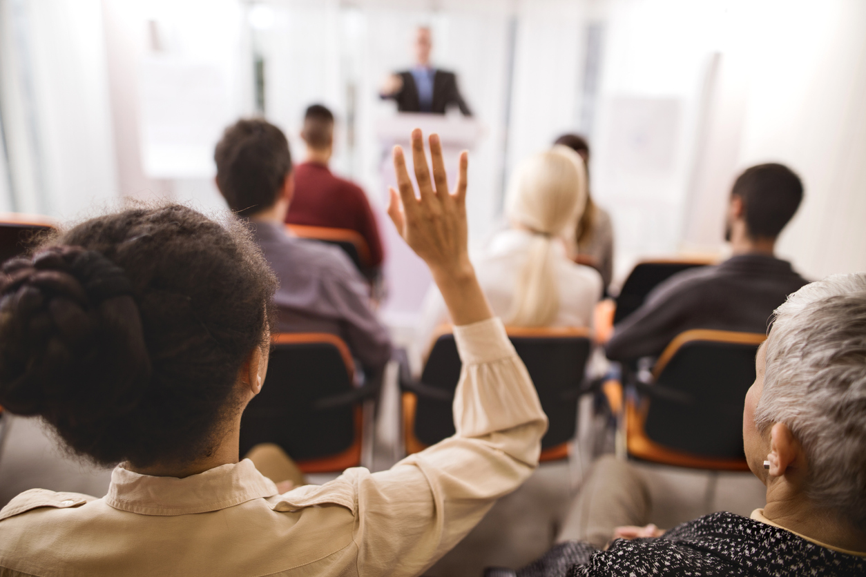 Rear view of a businesswoman raising her hand to ask the question on education event.