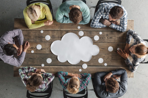 business teamwork brainstorming planning meeting concept, people sitting around the table with white paper shaped like dialog cloud