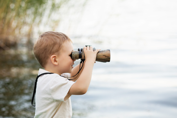 Little boy looking through binoculars on river bank