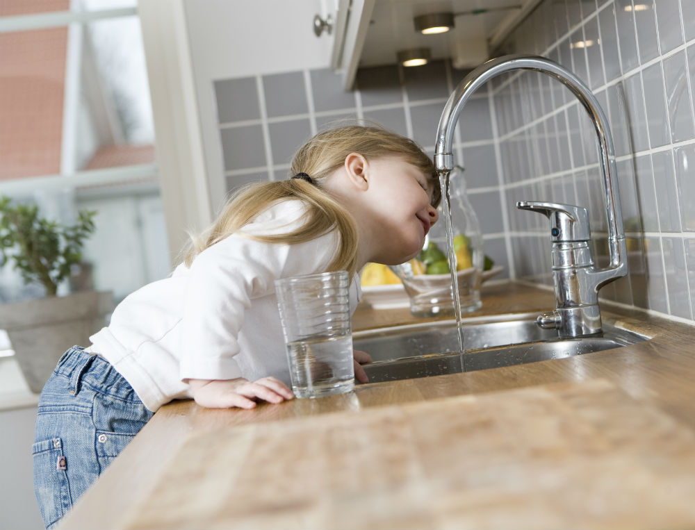 girl drinking from kitchen sink tap