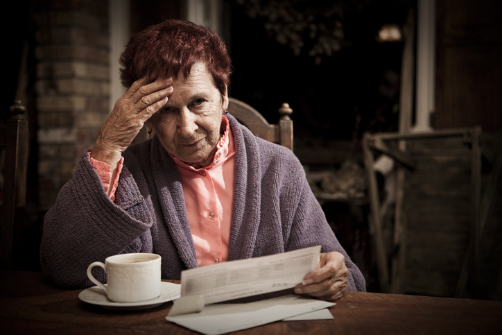 An elderly woman seated at the table with a cup of coffee distressed over the costs of her bills.