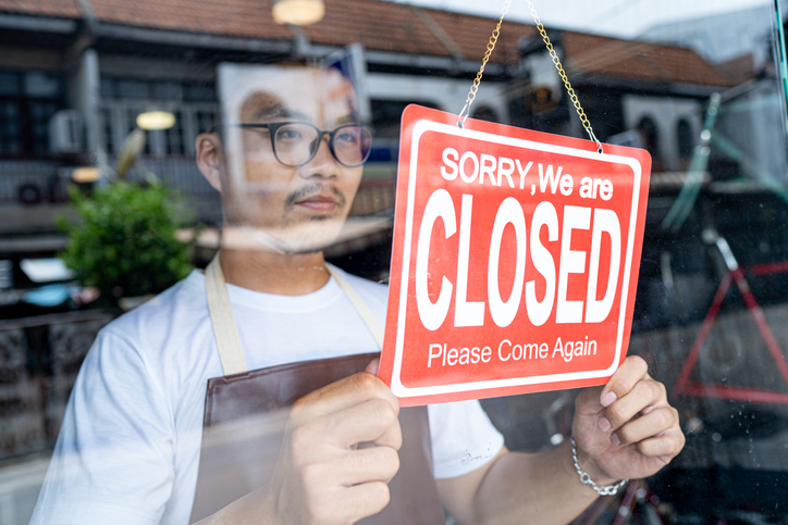 The owner of a small business shop puts up a closed sign in door window.