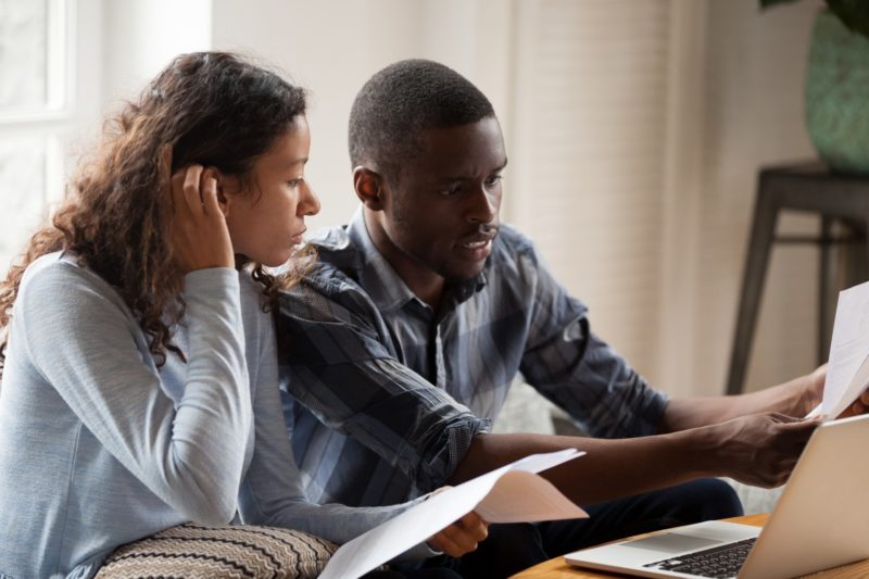 African Millennial couple sitting on sofa looking at bills