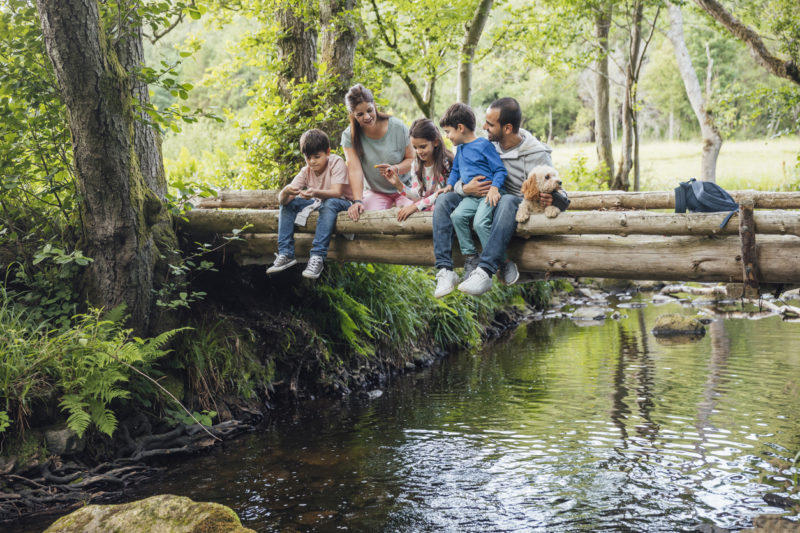 Family and dog sitting on bridge looking into river