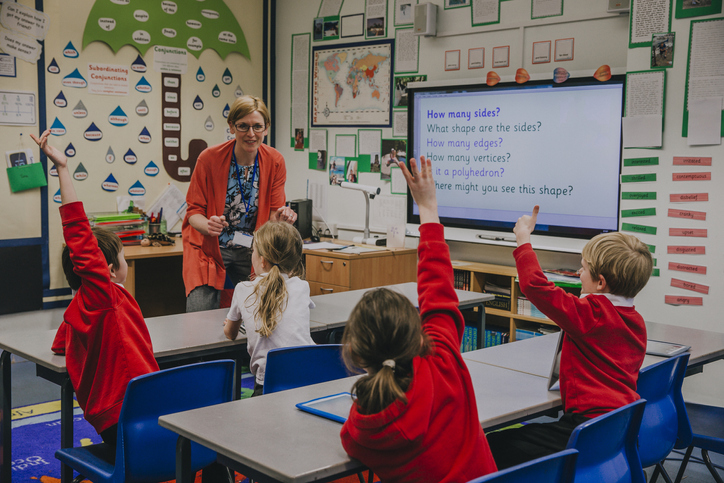 Primary school students with hands in air. Teacher asking a question