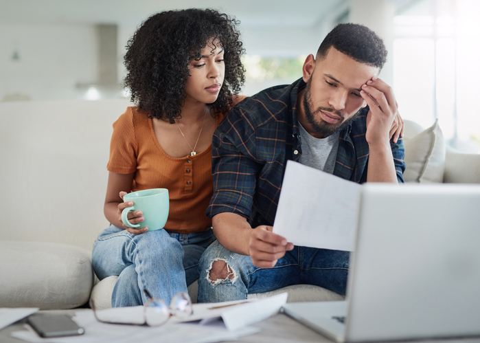Couple sitting on sofa looking stressed over their bills