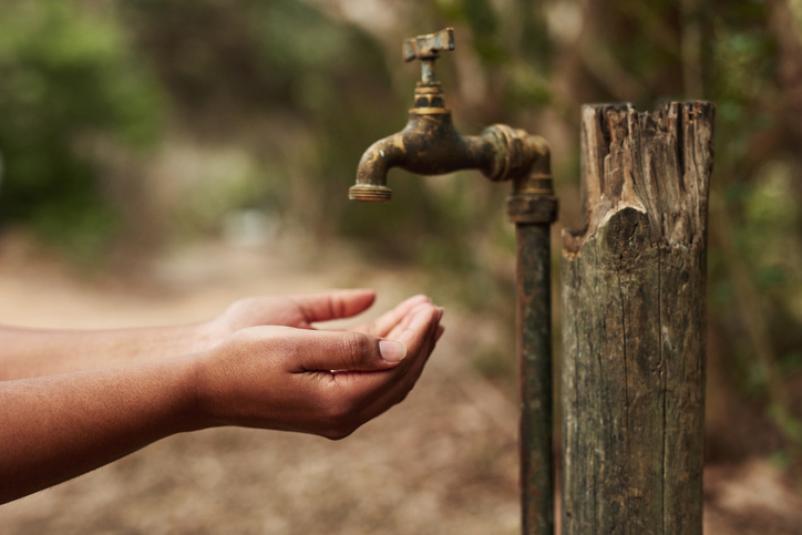 A woman holing her hands under an outdoor tap that is not running