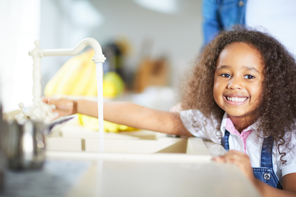 A mixed race little girl turns on a kitchen sink tap