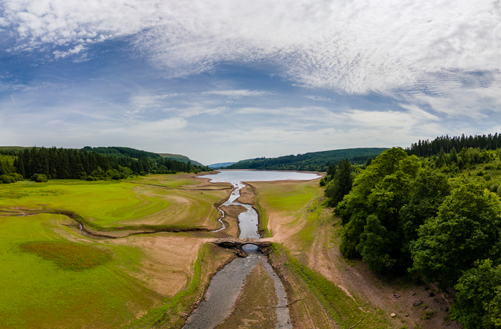 Aerial view of a near empty reservoir and old bridge during a UK heatwave (Llwyn Onn, Wales)