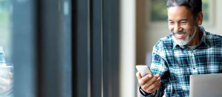 happy mature asian or hispanic man looking at smartphone smiling positive