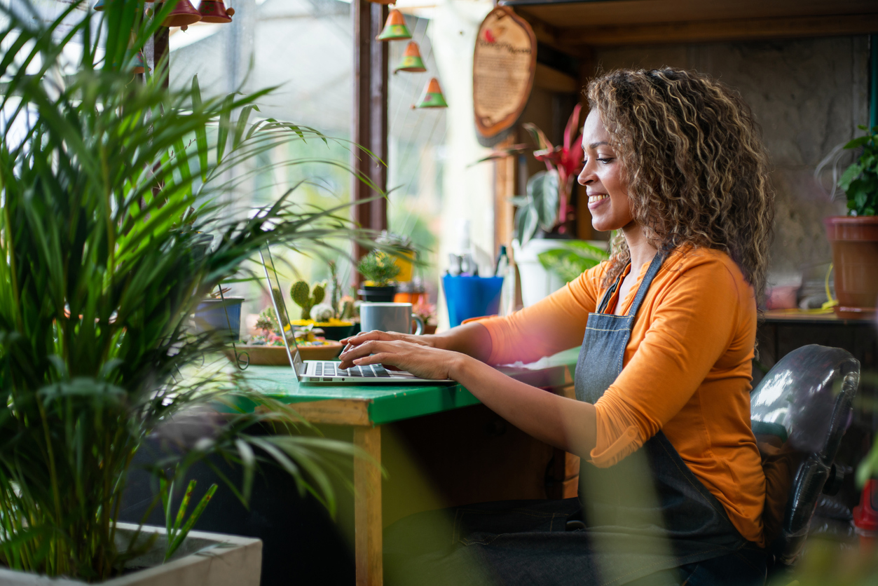 Happy Latin American woman working at her flower shop using a laptop computer