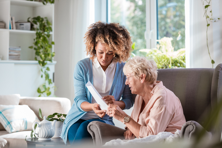 Female home caregiver supporting senior woman in her house, explaining her documents.