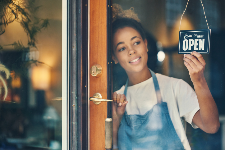 young woman hanging an open sign on the window of a cafe