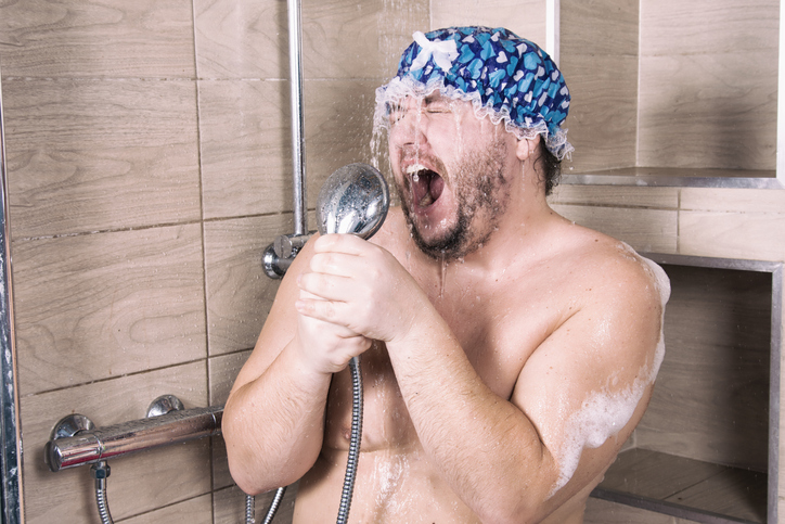 Funny man singing in the shower wearing a blue shower cap.