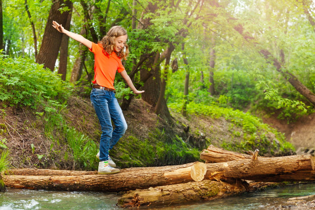 Child balancing on a log as they cross a stream