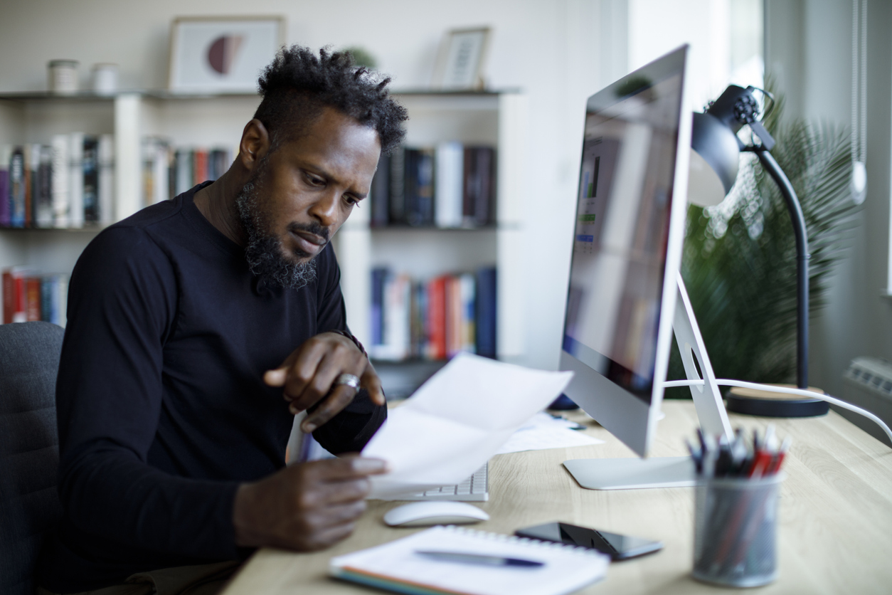 A black man looks at a bill while working at his desk.