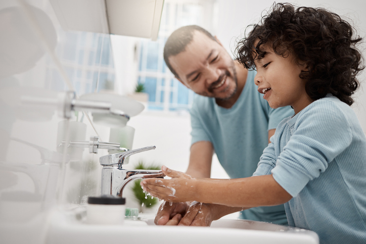 A father helping his son wash his hands and face at a tap in a bathroom at home