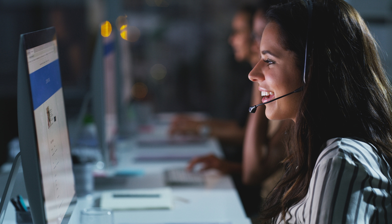 young female call center agent working late in the office with her colleagues in the background