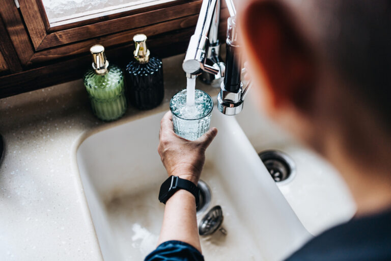 View over the shoulder of a man filling a glass with water in the kitchen sink