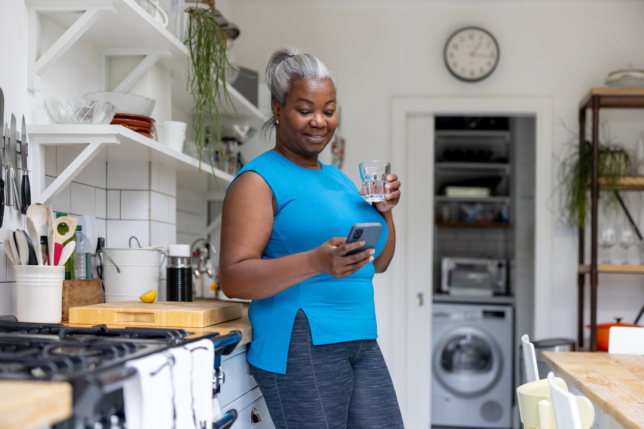 Happy woman drinking water and checking her cell phone after her home workout