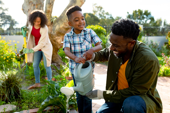 Happy black father, mother and son watering plants together.