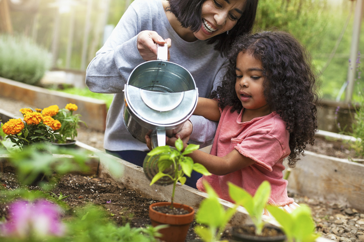 Mother and daughter watering potted plant at community garden