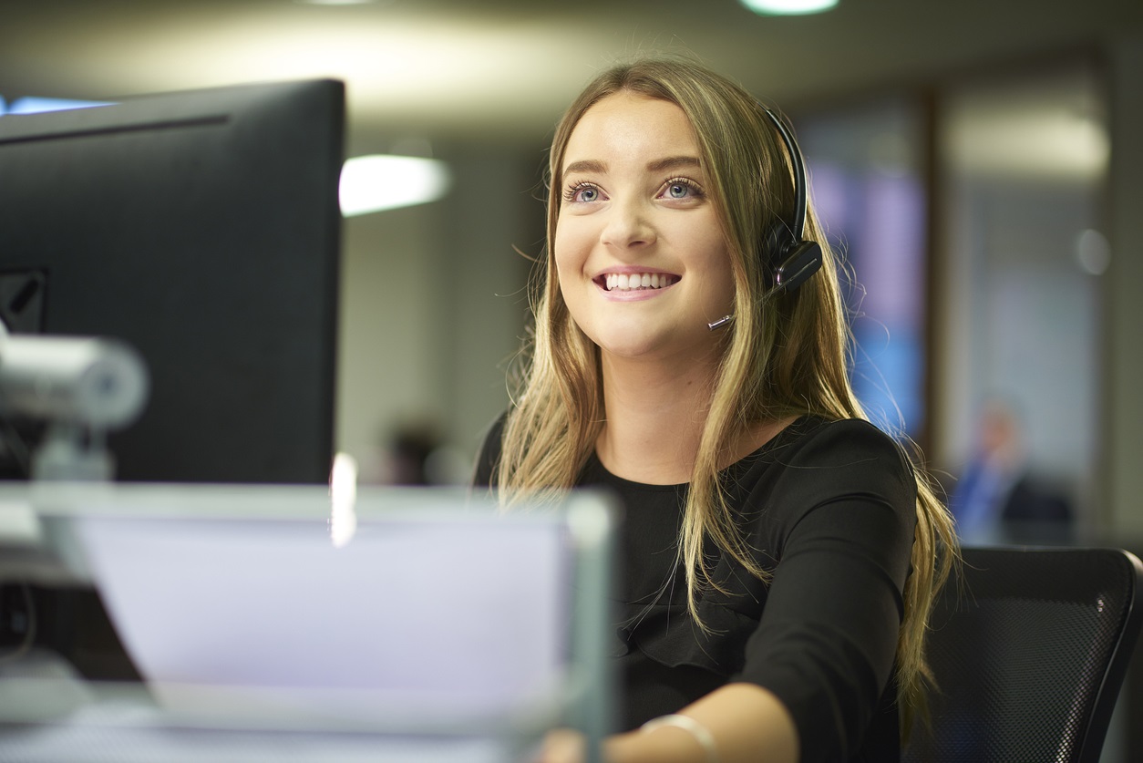 Office worker sits at her desk and speaks on her telephone headset.