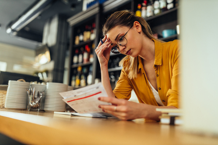 Owner of a restaurant checking financial business documentations while standing behind counter