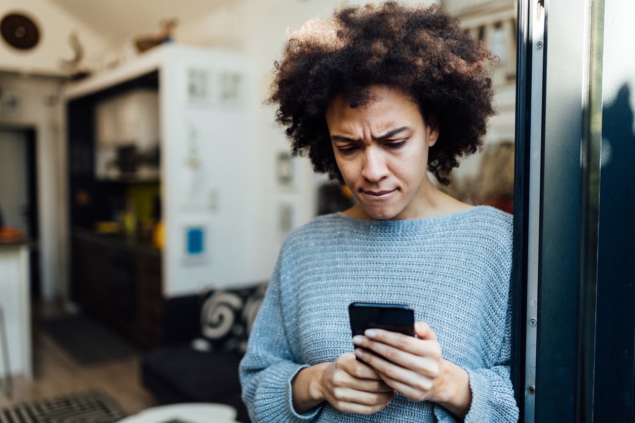 Young African American woman reading some bad news at home on her smart phone app, having a worried look on her face