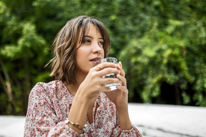 Woman sitting at the terrace on a sunny day drinking a fresh glass of water