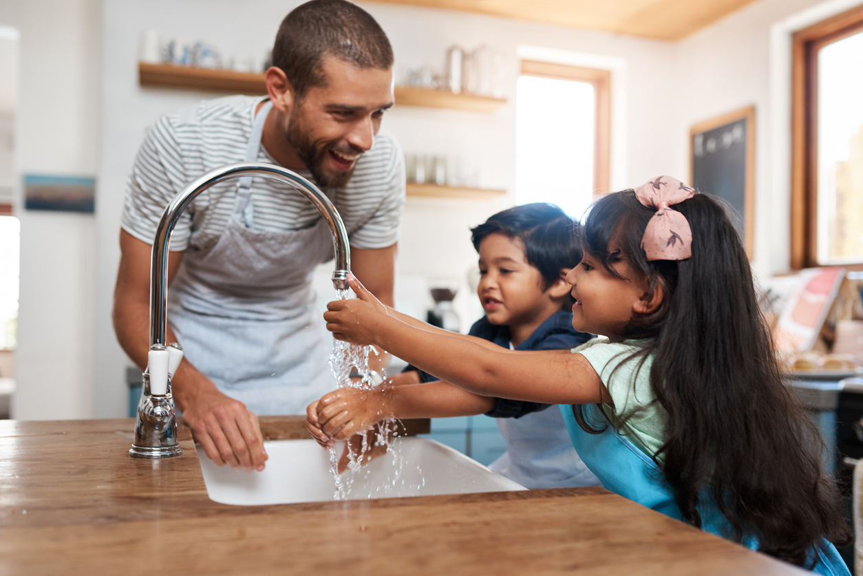 A man and his two children are washing their hands in the kitchen basin.