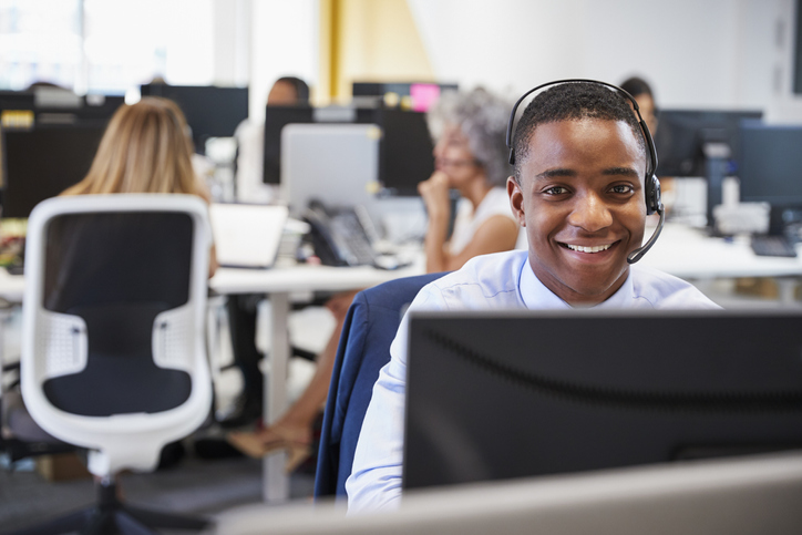 Young man working at computer with headset in busy office