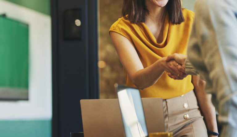 business women shaking hands. One wearing a bright yellow top
