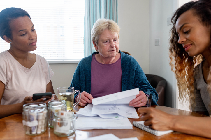 Three people sitting at a table reviewing financial documents together, with one person offering supportive guidance.
