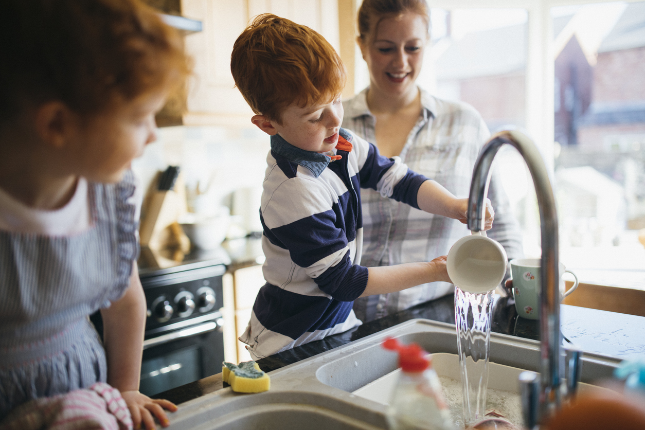 Two children and their mother are washing the dishes in the kitchen sink.