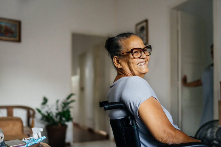 A happy elderly lady sits smiling in her wheelchair at home.