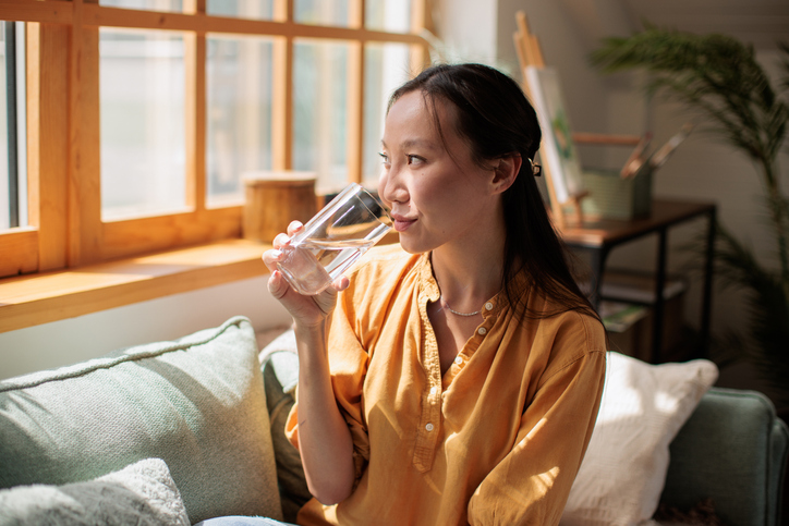 woman drinking water while sitting on a sofa in a cozy living room at home.