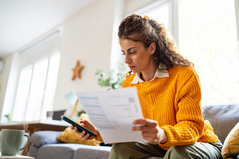woman wearing yellow jumper using mobile phone to calculate bill