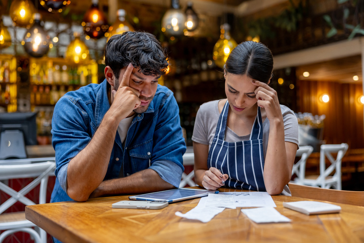 Business owner and waitress looking worried at paperwork