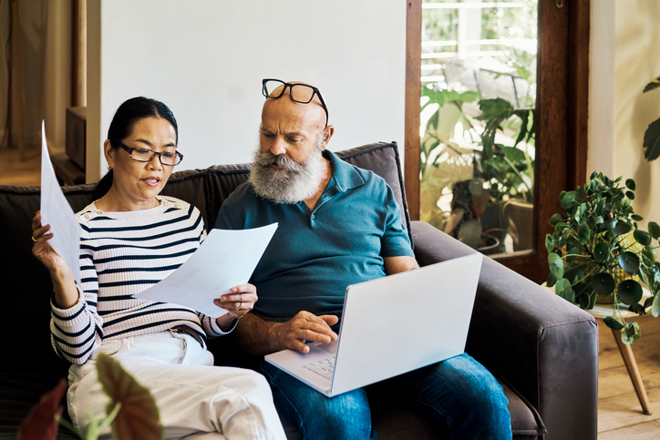 Senior interracial couple using a laptop and going through paperwork on sofa