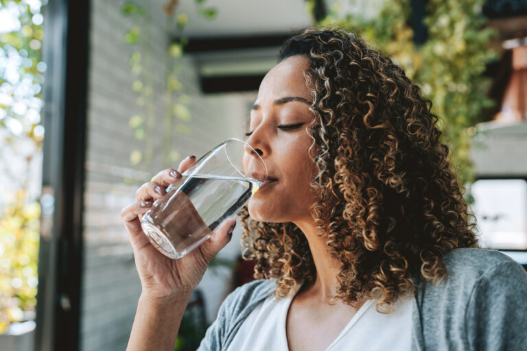 Woman stands at the kitchen sink drinking from a glass of water
