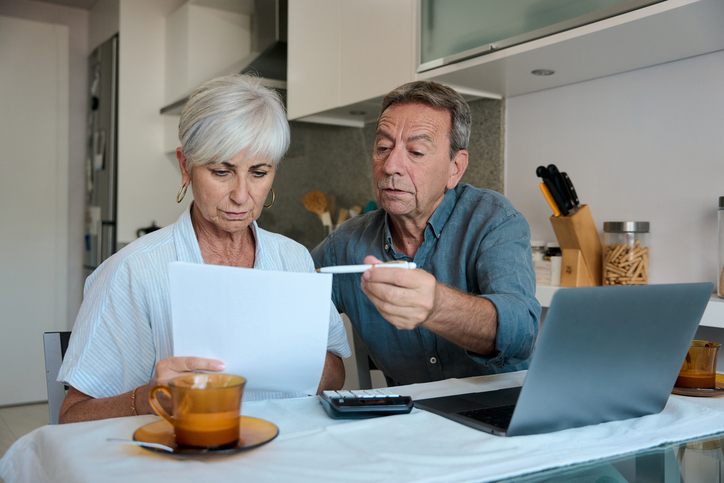 Worried senior couple checking domestic bills and calculating home finances sitting at the kitchen table