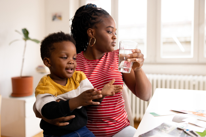 Mother holding her son while drinking a glass of water at home