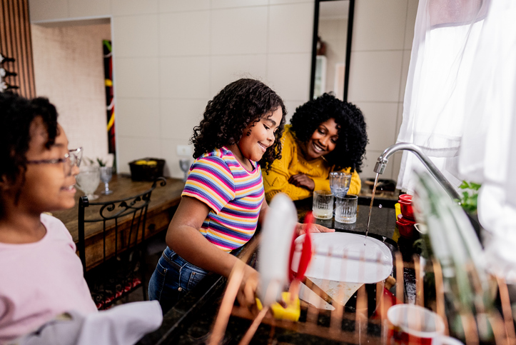 Girl washing dishes with her mother and sister in the kitchen at home