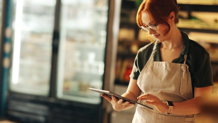Happy supermarket owner using a digital tablet while standing in her grocery store.